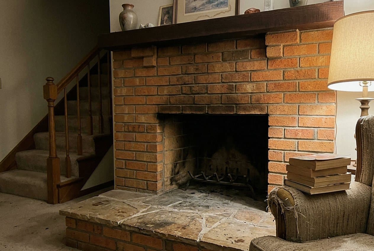 Dated brick fireplace beside a carpeted staircase